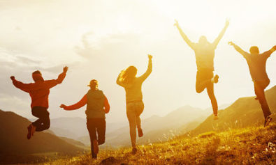 Group of five happy friends is running and jumping in sunset light on background of mountains. Happiness and friendship concept